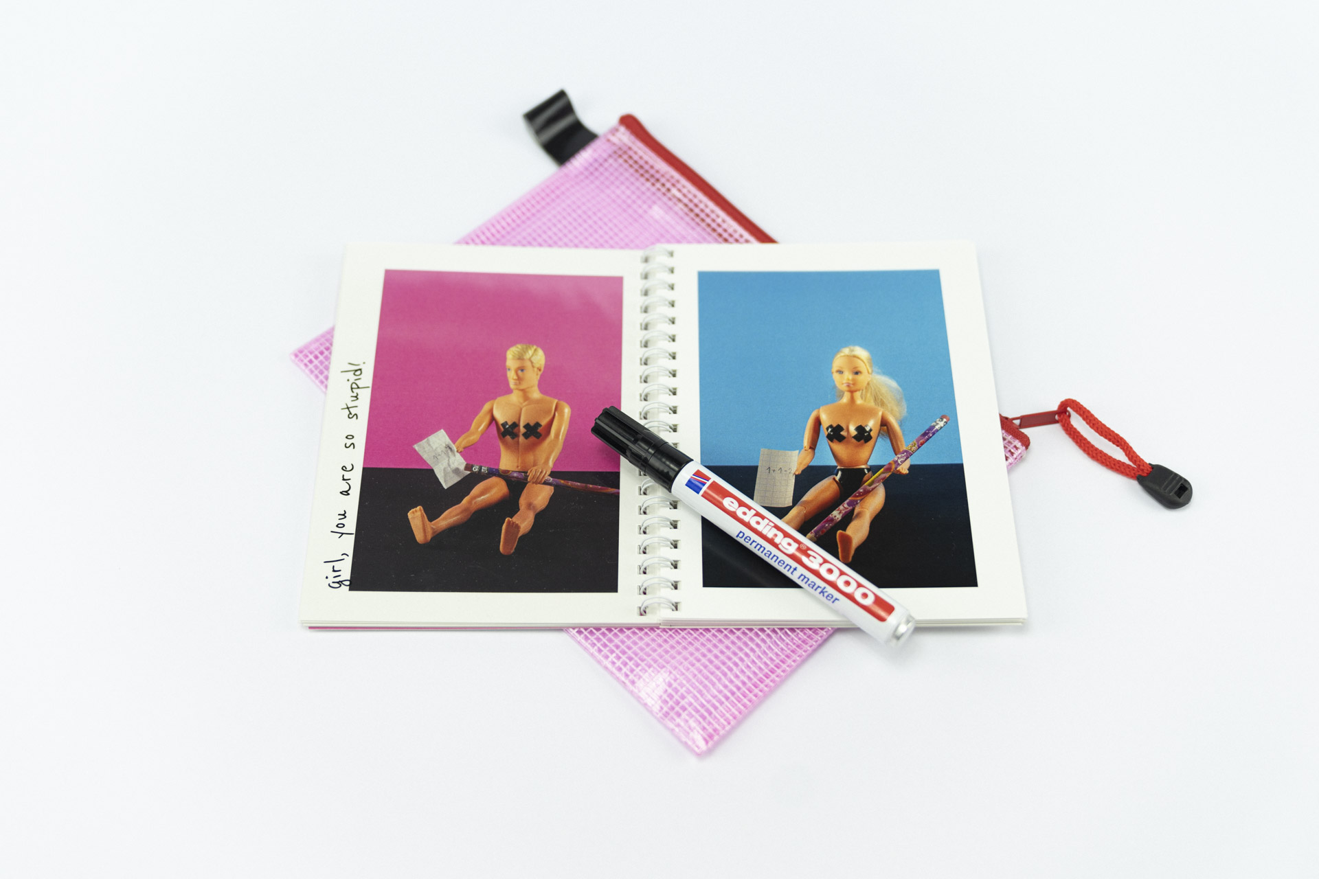 Detailaufnahme eines Fotobuchs mit dem Titel The Blond Stupid Boy auf weißem Hintergrund mit einer geöffneten Doppelseite mit jeweils vollflächigen Bildern von Barbie und Ken gegenübergestellt