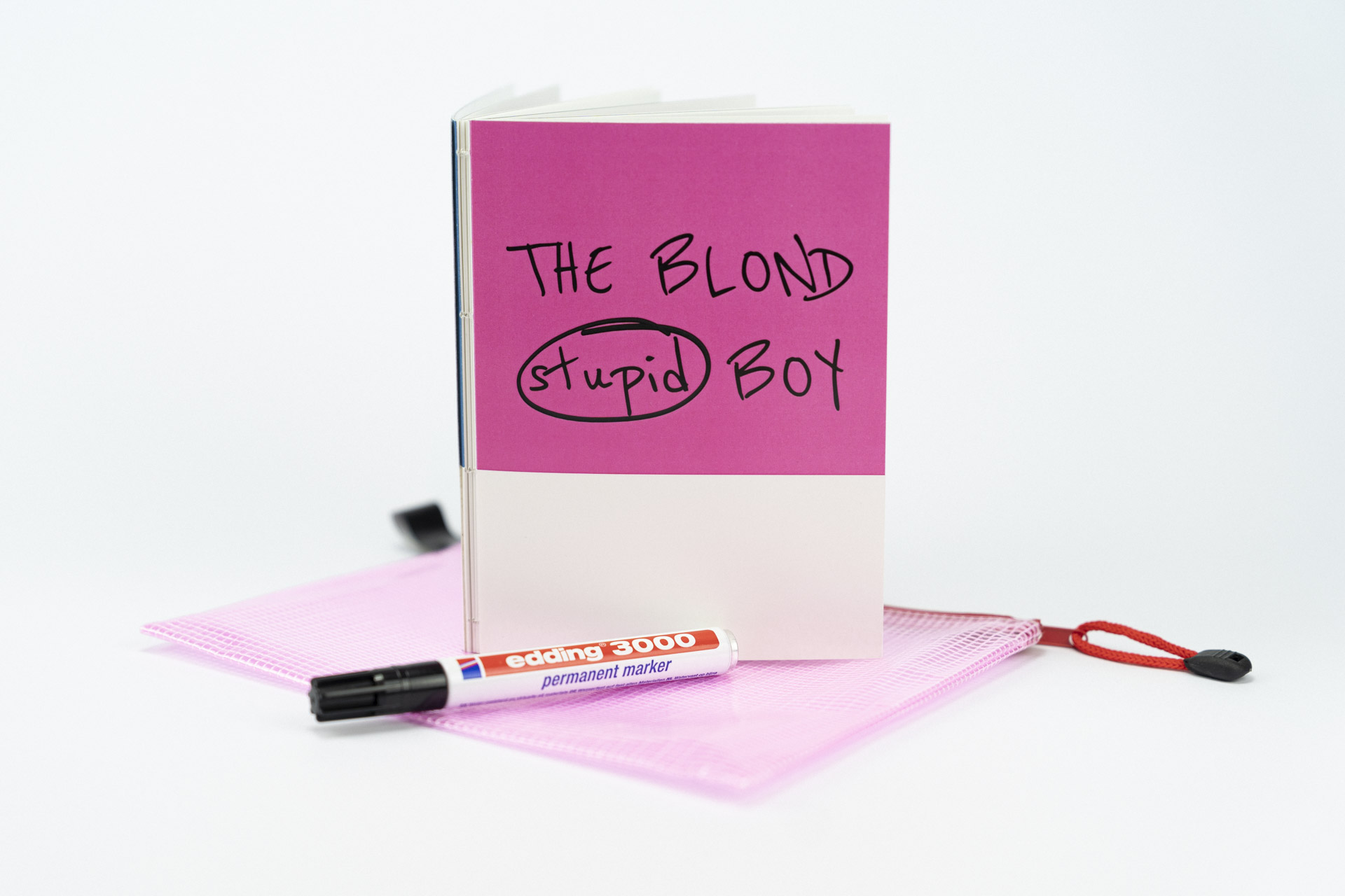Nahaufnahme eines aufgestellten Fotobuchs mit dem Titel The Blond Stupid Boy auf weißem Hintergrund mit einem Edding