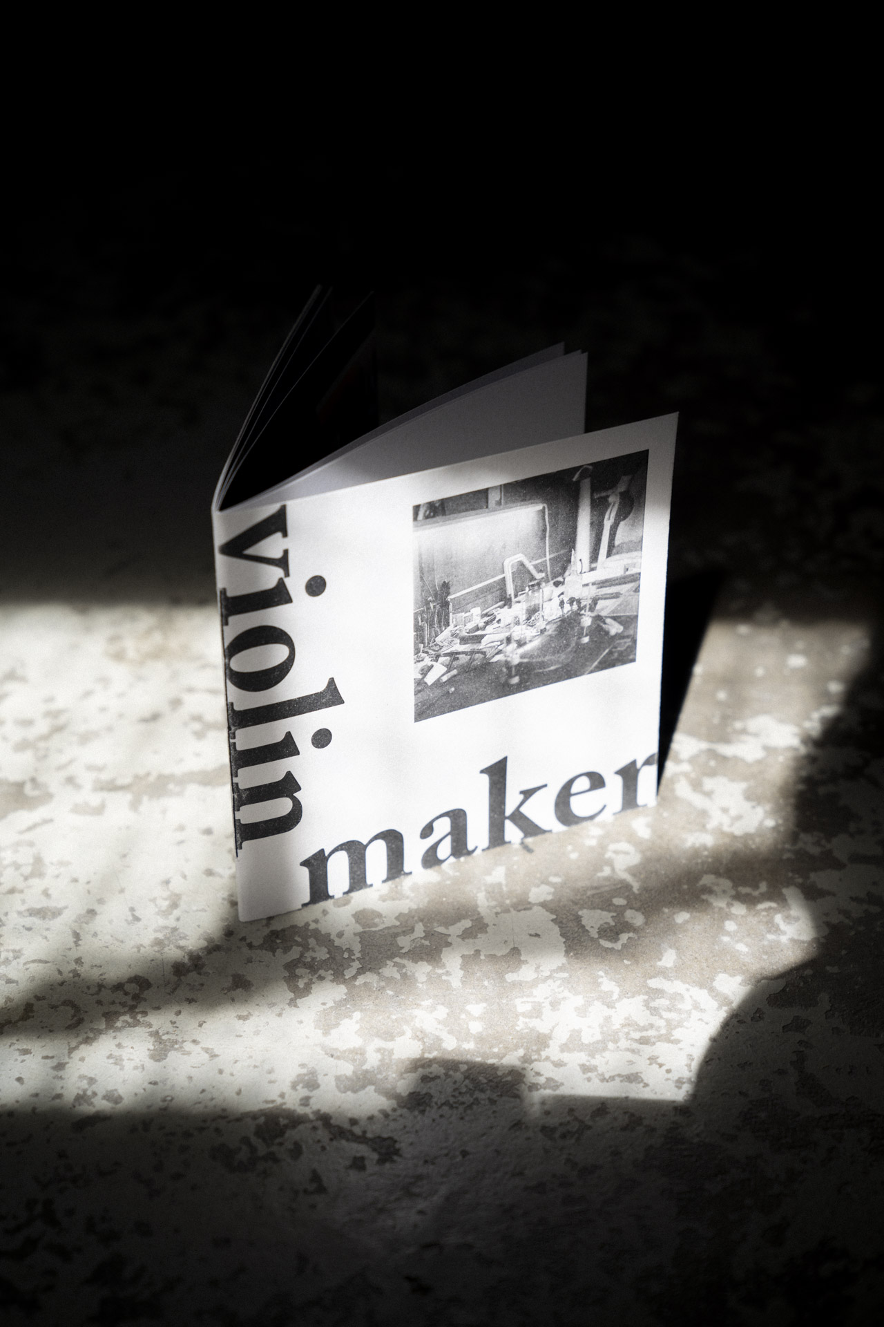 Umschlag des Violin Maker Fotobuch auf einem rustikalen Steinboden mit Schatten.