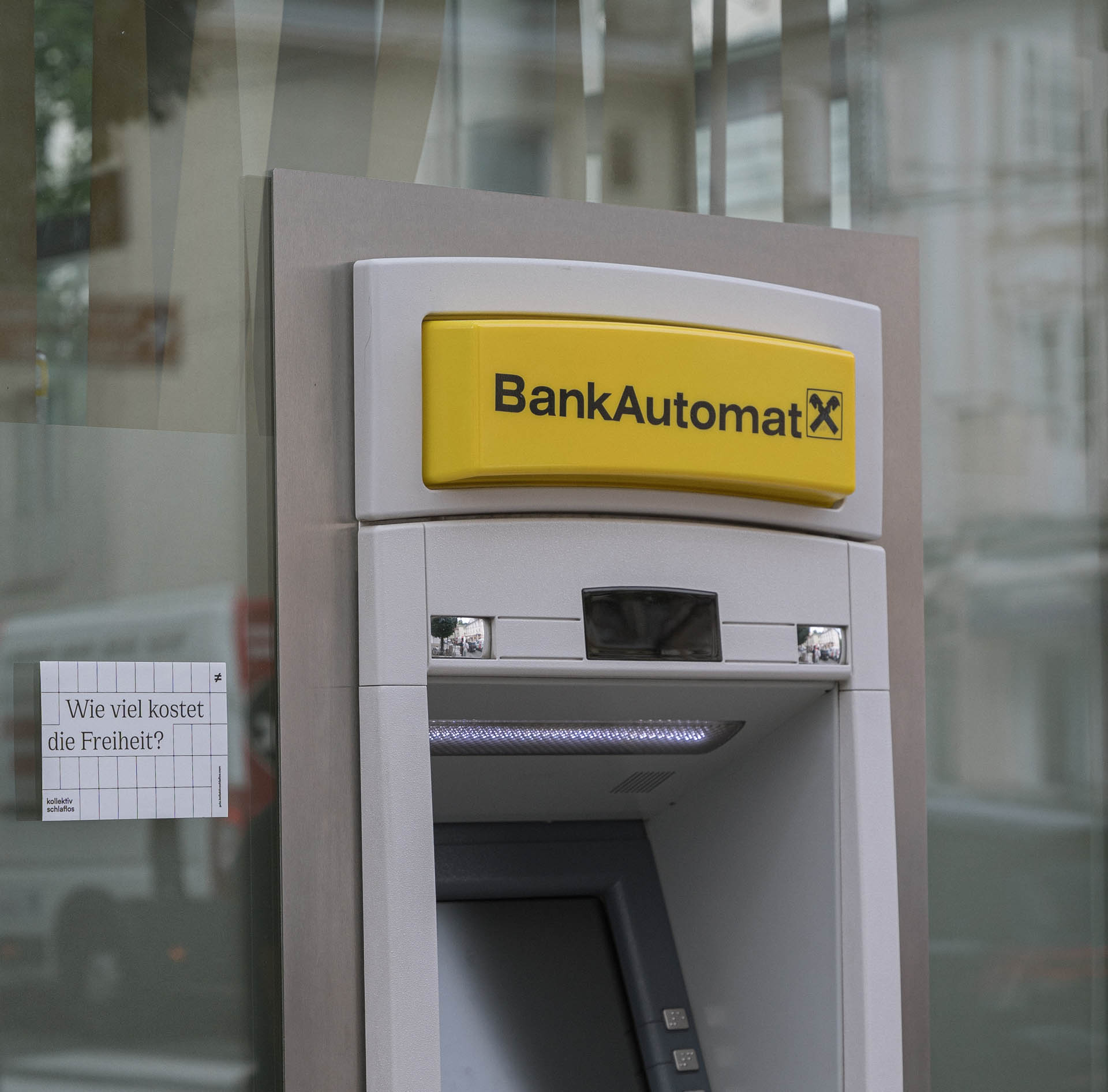 Bankomat mit einem Sticker daneben angebracht, welcher die Frage Wie viel kostet die Freiheit stellt.