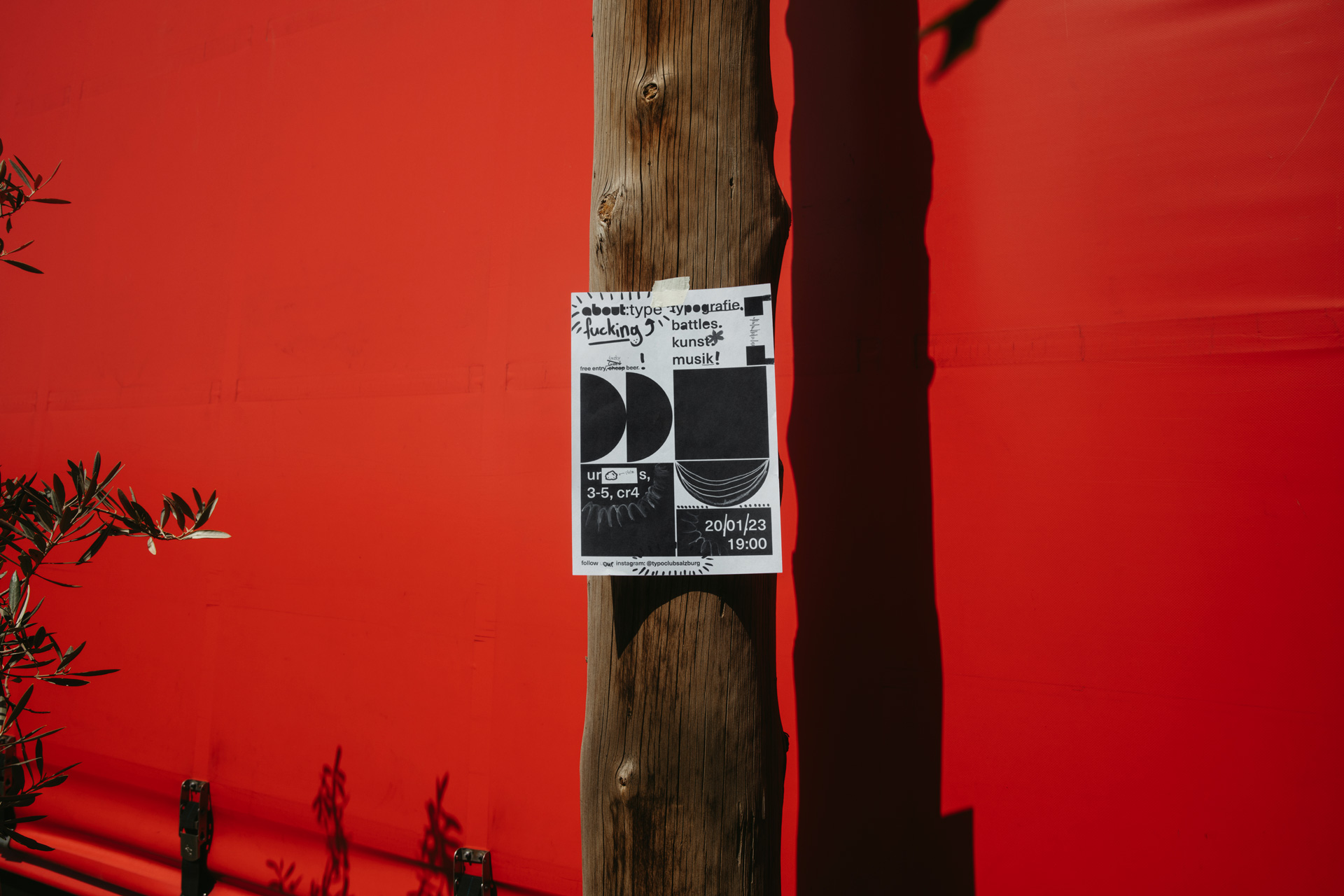 Analog und digital gestaltetes Plakat des Typoclub Salzburg auf einem Baumstamm vor einer roten Wand