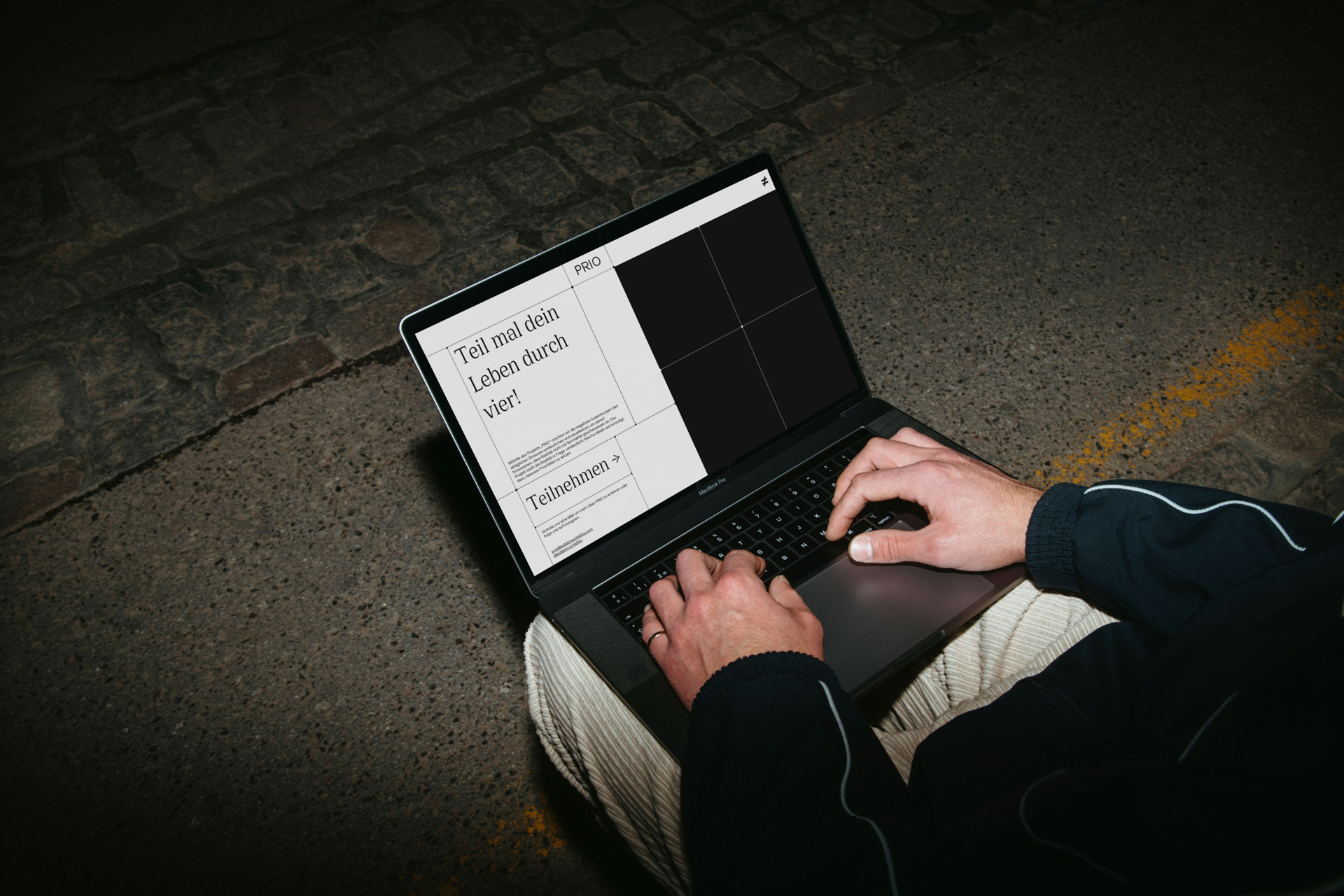 Nahaufnahme eines Laptosp auf den Beinen einer männlichen Person an einer Bushaltestelle. Laptop zeigt die Startseite der PRIO Datenvisualisierung an.